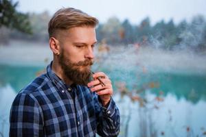 The bearded man smokes. Handsome stylish man in plaid shirt with cigarette. photo