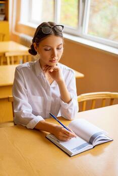 cute student sitting with a notebook at the Desk by the window, thoughtful view photo
