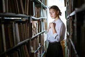 hermosa estudiante se encuentra entre las filas de la biblioteca, foto