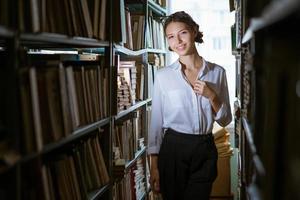Beautiful female student  stands between the rows in the library, photo