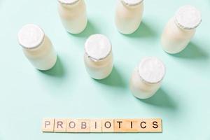 Small bottles with probiotics and prebiotics dairy drink on blue background. Production with biologically active additives. Fermentation and diet healthy food. Bio yogurt with useful microorganisms. photo