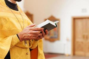 Iglesia Ortodoxa. cristiandad. manos de sacerdote sosteniendo el libro sagrado de la biblia en el fondo tradicional de la iglesia ortodoxa el día de la boda, la víspera de pascua o la celebración de navidad. religión fe orar símbolo foto