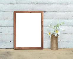 Vertical A4 Old Wooden Frame mockup near a bouquet of lilies stands on a wooden table on a painted white wooden background. Rustic style, simple beauty. 3d render. photo