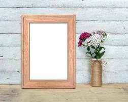 Old Wooden Frame mockup near a bouquet of sweet-william stands on a wooden table on a painted white wooden background. Vertical A4 Rustic style, simple beauty. 3d render. photo