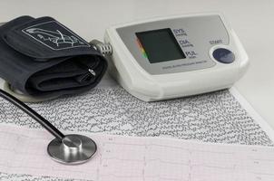 tonómetro eléctrico moderno y un estetoscopio en un gráfico de cardiograma. tensiómetro doméstico foto