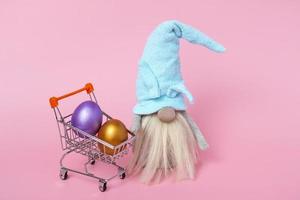 Festive banner. On a pink background, a gnome and Easter eggs in a cart. Closeup copy space photo