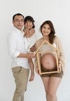 Pregnant Woman with Husband and Daughter Holding House Shape Wooden Figure and Standing Together photo