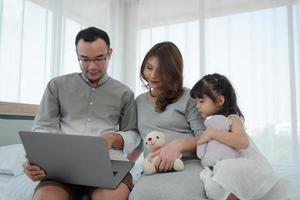 Pregnant Family With Young Daughter Watching Cartoon From Computer Together in Bedroom photo