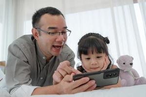 Father Watching Cartoon From Smartphone with Young Daughter in Bedroom photo