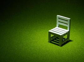 White wooden chair on artificial grass. Light shining down from above in the dark tone low key photo