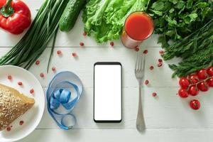 The smartphone lies on a table with diet vegetables. Place for your text. photo