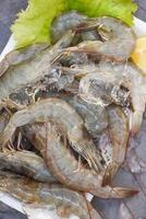 Fresh shrimp prawns for cooking with spices lemon vegetable salad lettuce on dark background in the seafood restaurant, Close up raw shrimps on plate plastic tray, top view photo