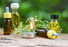 Aromatherapy herbal oil bottles aroma with flower leaves herbal formulations including wildflowers and herbs on wood - Scented candles essential oils natural on wooden and green leaf background photo