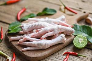 patas de pollo crudas frescas para sopa de comida cocida en el fondo oscuro de la cocina de la mesa, patas de pollo en una tabla de cortar de madera con hierbas y especias limón ajo kaffir hojas de lima foto