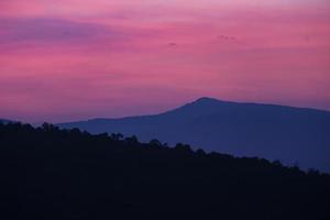 naturaleza paisaje fondo hermosa vista de la niebla de la mañana llenando los valles de colinas suaves capa de cordillera bosque azul oscuro amanecer y atardecer en montañas con cielo púrpura dramático foto