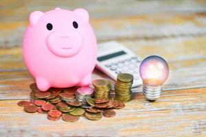 light bulb with light from the lamp and coin piggy bank on wooden table background - energy saving idea , power saving and the world concept photo