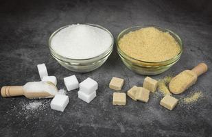 White and brown sugar cubes and heap of sugar on bowl and wooden scoop on table background photo