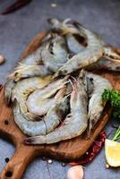 Fresh shrimp prawns for cooking with spices lemon garlic black pepper chili on wooden cutting board in the seafood restaurant, raw shrimps on dark plate