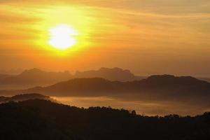 Nature landscape background beautiful view of the morning fog filling the valleys of smooth hills mountain range layer yellow forest sunrise and sunset in mountains with orange sky photo