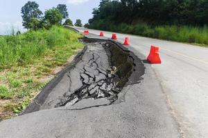 la carretera de asfalto se derrumbó y las grietas en la carretera - el derrumbe de la carretera se hundió con barreras de plástico cuesta arriba foto