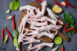 patas de pollo crudas frescas para sopa de comida cocida en el fondo oscuro de la cocina de la mesa, patas de pollo en una tabla de cortar de madera con hierbas y especias limón ajo kaffir hojas de lima foto