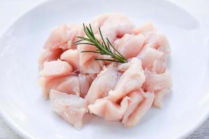 Pieces of raw chicken meat with rosemary - fresh raw cut chicken fillet on white plate background photo