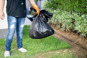 Woman holding black plastic trash bin bags of garbage on the pavement, clean environment concept. photo