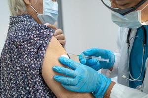 Elderly Asian senior woman wearing face mask getting covid-19 or coronavirus vaccine by doctor make injection. photo