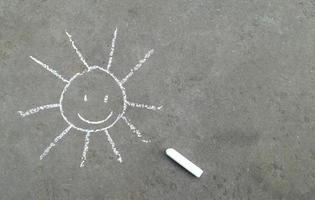 sun with a smile is drawn in chalk on the asphalt. banner with place for your text, copy space. children creativity, summer joy emotion photo