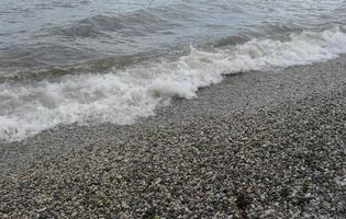 sea wave with foam on the shore with pebbles. background, banner, summer, travel photo