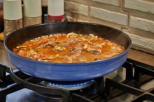 Veal tongue with tomato sauce, mushrooms and capers is fried in frying pan on gas stove. French gourmet cuisine