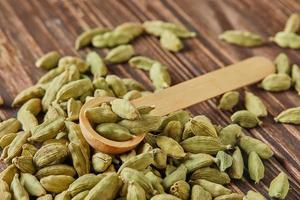 cardamomo verde con cuchara de madera esparcida sobre fondo de madera vintage foto