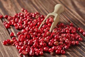 Red peppercorns with wooden spatula scattered on wooden vintage background photo