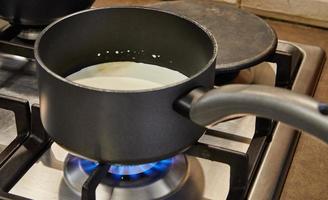 la crema se cocina en una cacerola en la estufa de gas para hacer pastel foto