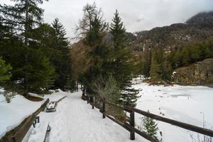 A snow covered pedestrian path that runs alongside a frozen mountain lake photo