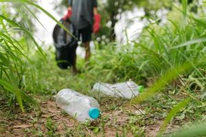 La mano del hombre del muchacho recoge la botella plástica en el bosque. concepto de medio ambiente. foto