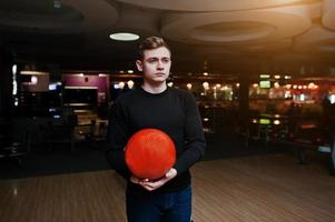 Young man holding a bowling ball standing against bowling alleys with ultraviolet light. photo