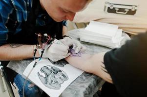 Tattoo master make tattoo for rocker man at tattoo salon photo