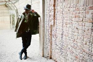 retrato de moda de hombre afroamericano negro con chaqueta de terciopelo verde, sombrero negro y capa de abrigo sobre sus hombros posado en el túnel del arco foto