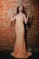 Full length shot of fashionable model girl at peach evening dress background brick wall. photo