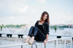 Portrait of gorgeous sexy brunette girl model sitting on the railing of the pier photo