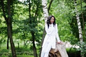 retrato de una elegante chica afroamericana negra sentada en un tocón en un parque verde foto