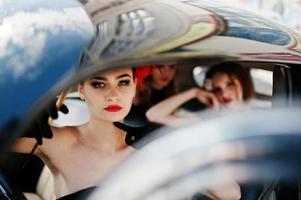 Three young girl in retro style dress seat on old classic vintage car. Amazing view of sexy women. photo