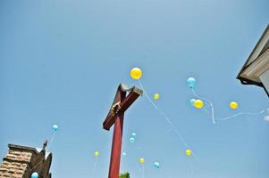Blue and yellow balloons at sky background cross at church. photo