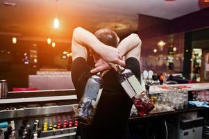 joven barman sosteniendo botellas de cóctel en el bar foto