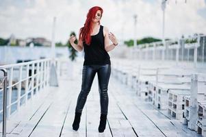 Young red haired girl at black clothes posed on the pier photo