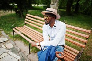 hombre negro rico sentado en un banco con gafas de sol doradas y sombrero foto