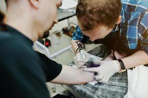 el maestro del tatuaje hace un tatuaje para un hombre rockero en el salón de tatuajes foto