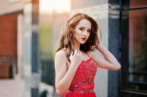 Close up portrait of fashionable girl at red evening dress posed background mirror window of modern building photo