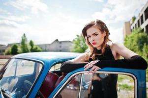 Portrait of beautiful fashion girl model with bright makeup in retro style leaned on a vintage car door. photo